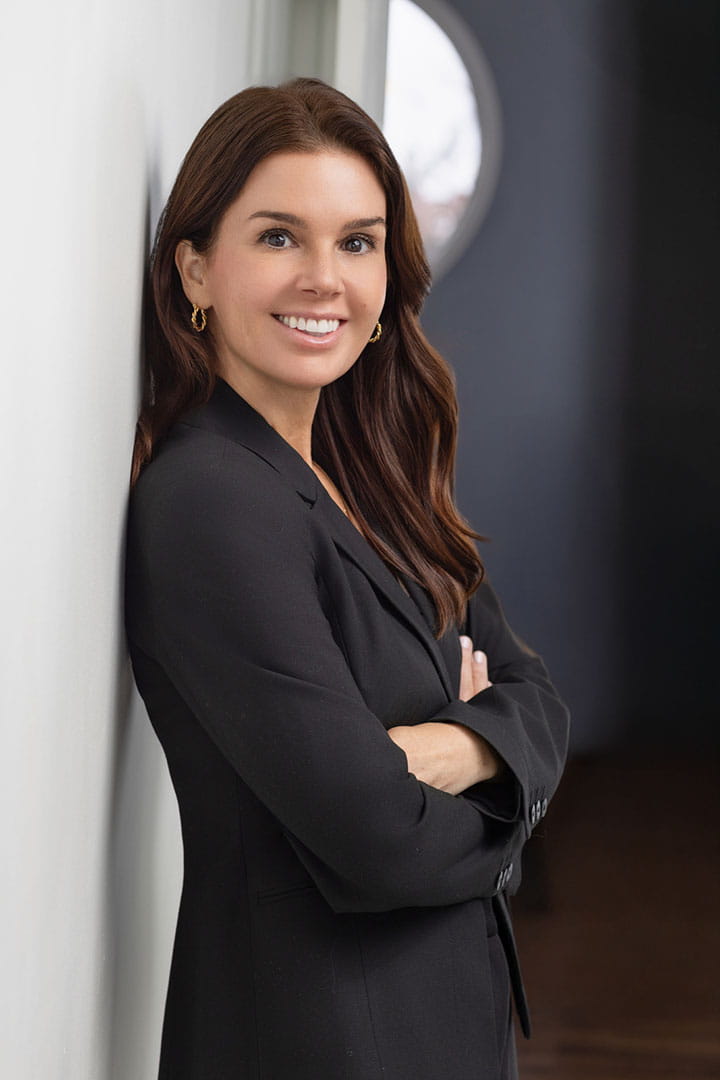 Jamie Salvetti in a black suit, standing confidently with arms crossed against a wall, in a stylish interior setting.
