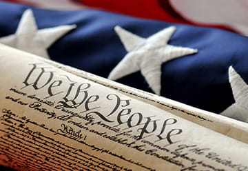 Close-up of the U.S. Constitution scroll, with a backdrop of the American flag, symbolizing immigration rights and law.