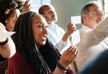 Diverse group of people engaged in a discussion, some holding up cards, showcasing participation and community interaction.