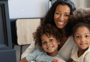 Smiling mother with two children, sitting together in a cozy home setting, conveying family unity and warmth.